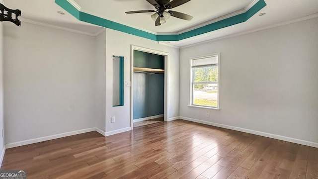 unfurnished bedroom with a closet, baseboards, crown molding, a raised ceiling, and wood finished floors