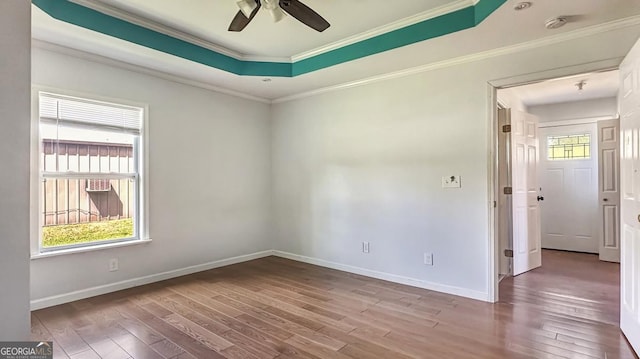 spare room featuring crown molding, a tray ceiling, a ceiling fan, wood finished floors, and baseboards