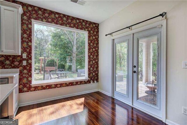unfurnished dining area with dark wood-style flooring, visible vents, plenty of natural light, and wallpapered walls