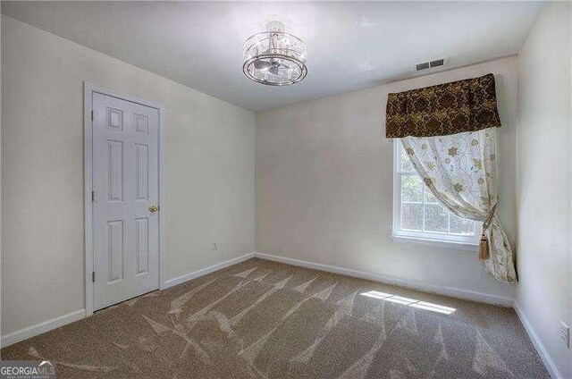 unfurnished room with a chandelier, carpet flooring, visible vents, and baseboards