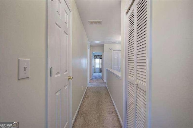 hall with visible vents, baseboards, attic access, and carpet flooring