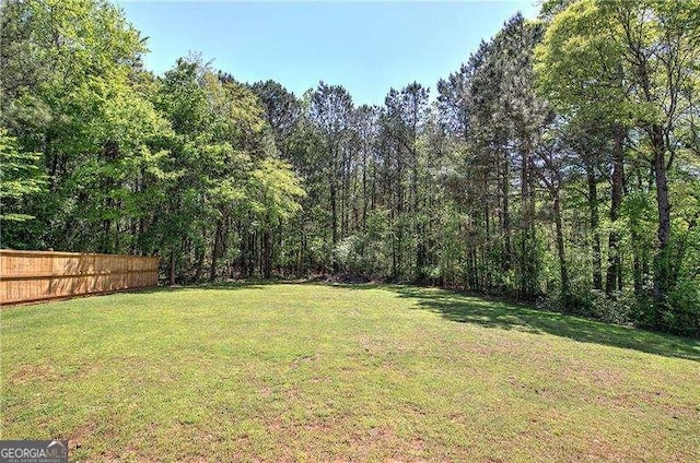 view of yard featuring a wooded view and fence