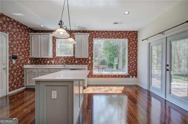 kitchen with baseboards, wallpapered walls, light countertops, dark wood finished floors, and a sink