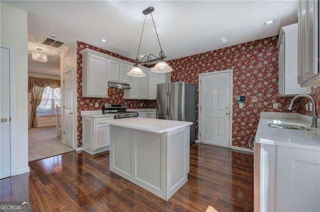 kitchen featuring dark wood-style flooring, a sink, under cabinet range hood, wallpapered walls, and stainless steel appliances
