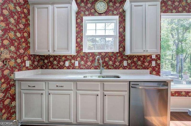 kitchen featuring light countertops, wallpapered walls, stainless steel dishwasher, and a sink