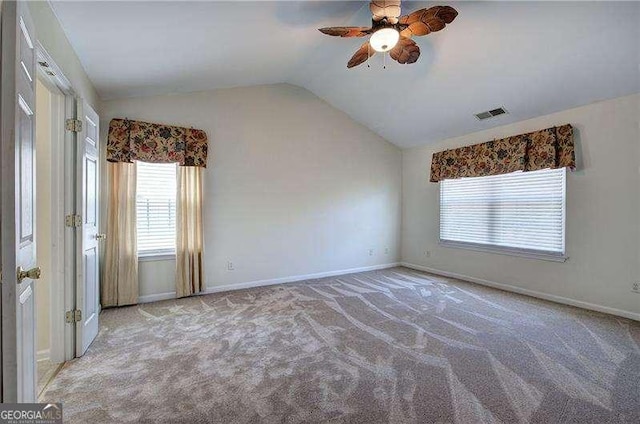 carpeted spare room with visible vents, vaulted ceiling, a ceiling fan, and a healthy amount of sunlight