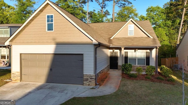 traditional-style house with an attached garage, a shingled roof, stone siding, and driveway