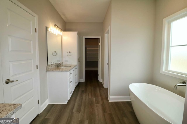 full bath with vanity, a spacious closet, wood finished floors, a freestanding bath, and baseboards