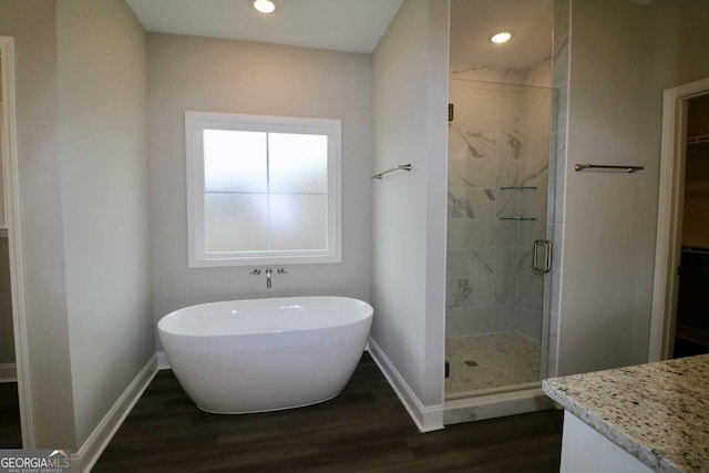 bathroom featuring baseboards, a freestanding tub, a spacious closet, a shower stall, and wood finished floors