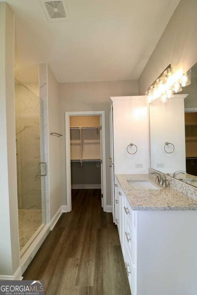 full bathroom featuring a shower stall, wood finished floors, a walk in closet, and visible vents