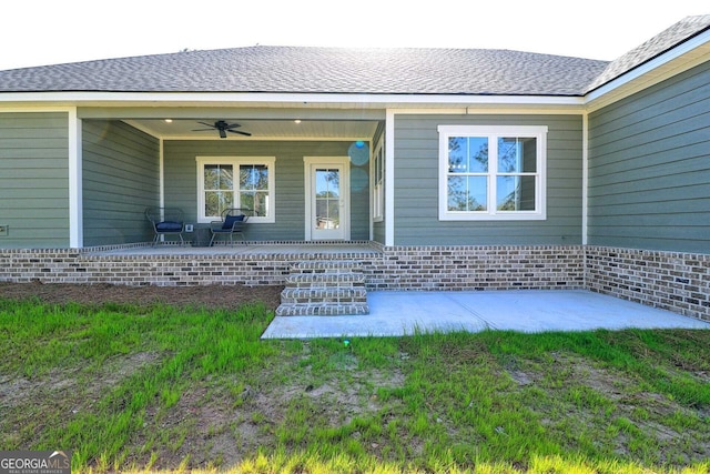 property entrance featuring a lawn, brick siding, ceiling fan, a shingled roof, and covered porch
