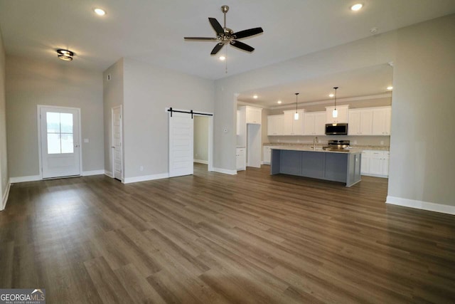 unfurnished living room featuring dark wood-type flooring, baseboards, and a barn door