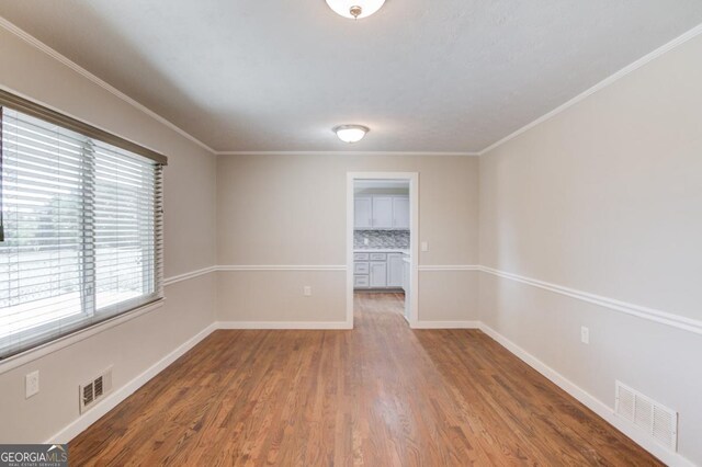 empty room with baseboards, visible vents, wood finished floors, and crown molding