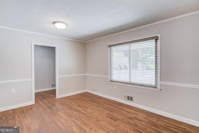 spare room with baseboards, visible vents, wood finished floors, and ornamental molding