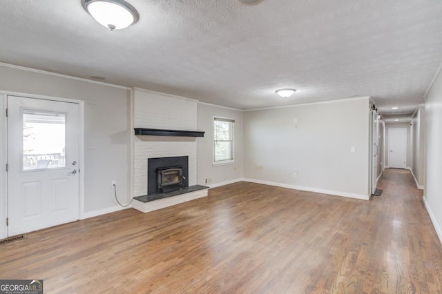 unfurnished living room with a wood stove, crown molding, baseboards, a textured ceiling, and wood finished floors