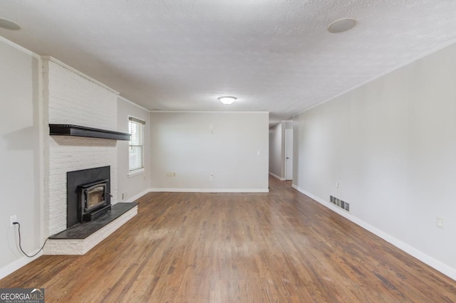 unfurnished living room featuring a wood stove, visible vents, wood finished floors, and baseboards