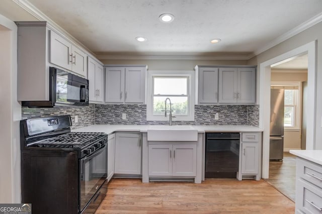 kitchen featuring a sink, crown molding, black appliances, light countertops, and gray cabinetry