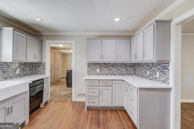 kitchen with light countertops, ornamental molding, dishwasher, light wood finished floors, and visible vents