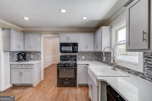 kitchen with tasteful backsplash, a sink, light countertops, black appliances, and light wood finished floors