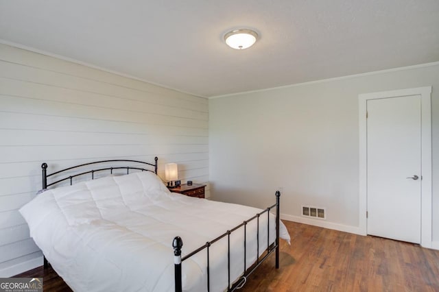 bedroom with crown molding, visible vents, wood finished floors, and baseboards