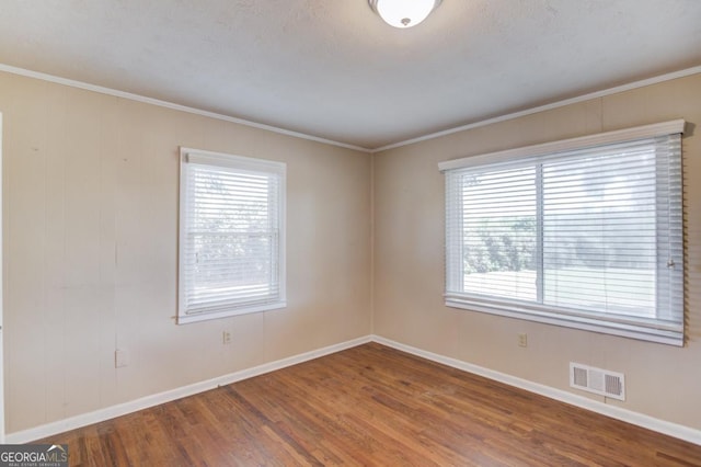 unfurnished room with baseboards, visible vents, wood finished floors, and crown molding