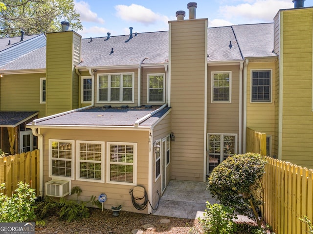rear view of house featuring a patio, a chimney, fence, and a shingled roof