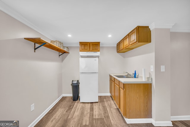 kitchen with a sink, ornamental molding, light countertops, freestanding refrigerator, and light wood finished floors