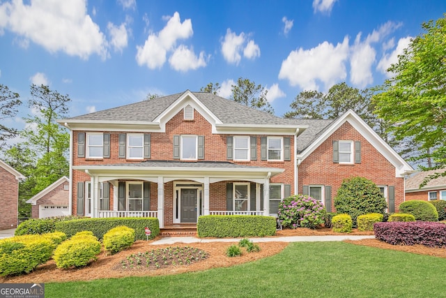 view of front of property featuring brick siding, a front yard, a porch, and roof with shingles