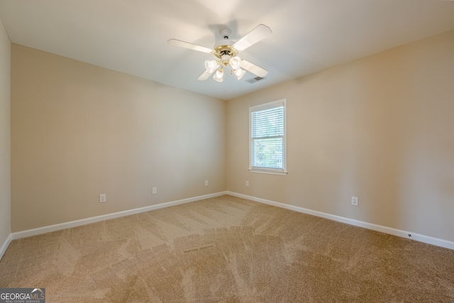 spare room with light colored carpet, baseboards, a ceiling fan, and visible vents