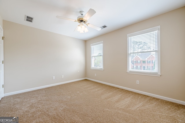 spare room featuring visible vents, baseboards, a ceiling fan, and light carpet