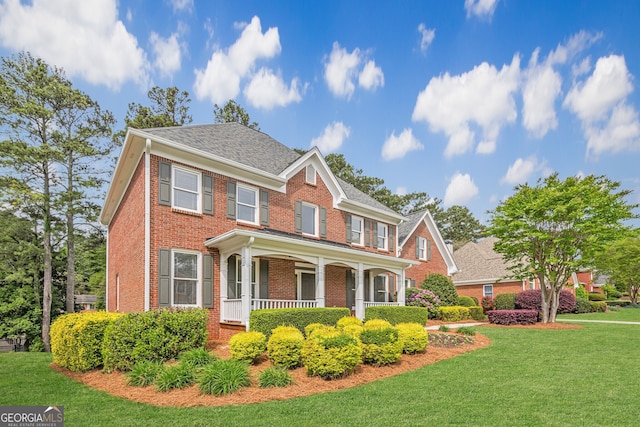 view of front facade with a porch, a front lawn, and brick siding