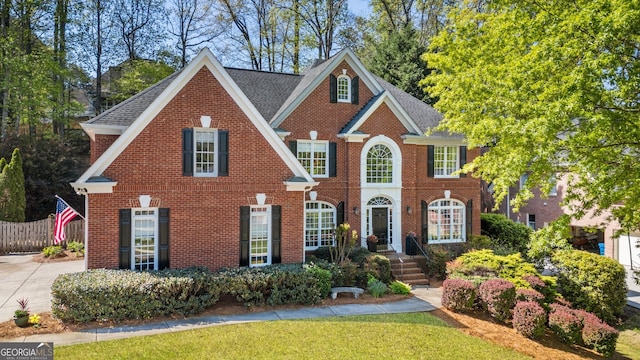 view of front facade featuring brick siding, fence, and a shingled roof