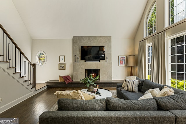 living room featuring baseboards, stairway, dark wood finished floors, high vaulted ceiling, and a tile fireplace