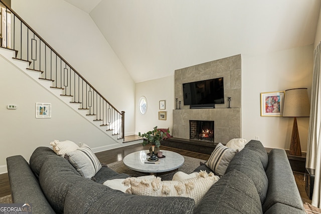 living room with baseboards, stairway, wood finished floors, high vaulted ceiling, and a tile fireplace
