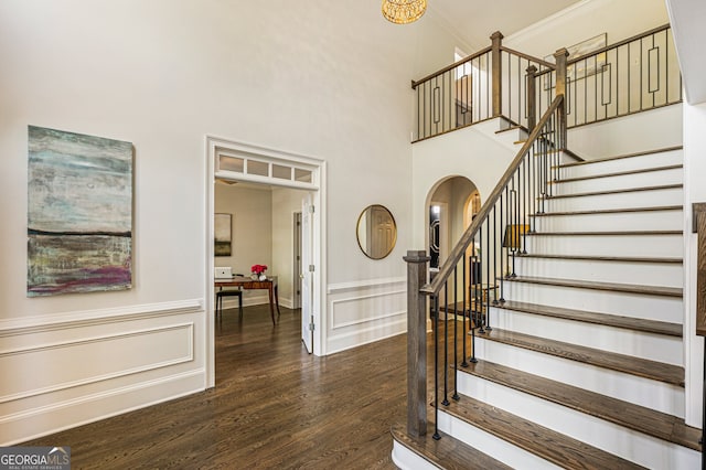 stairway with arched walkways, a towering ceiling, wainscoting, and wood finished floors