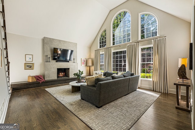 living area with a healthy amount of sunlight, high vaulted ceiling, dark wood-style floors, and a tile fireplace
