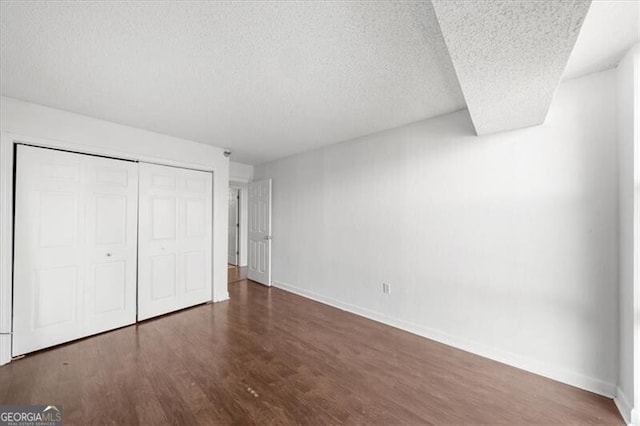 unfurnished bedroom featuring a closet, a textured ceiling, baseboards, and wood finished floors