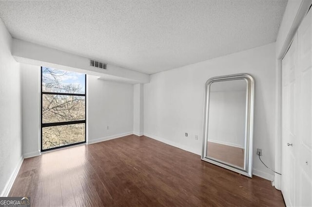 interior space featuring visible vents, a textured ceiling, baseboards, and wood finished floors