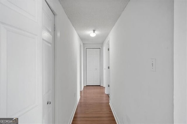corridor with dark wood-style flooring, baseboards, and a textured ceiling