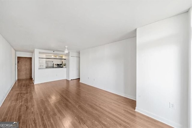 unfurnished living room with wood finished floors, baseboards, and a ceiling fan