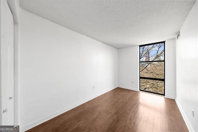 spare room featuring dark wood-style flooring, a textured ceiling, and baseboards