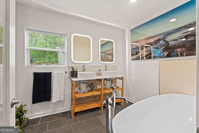 full bathroom featuring a freestanding tub, baseboards, double vanity, tile patterned flooring, and a sink