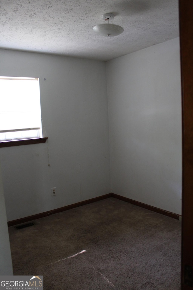 empty room featuring a textured ceiling, carpet, visible vents, and baseboards