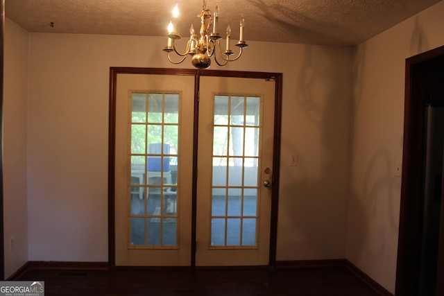 doorway to outside with baseboards, a textured ceiling, a chandelier, and dark wood finished floors