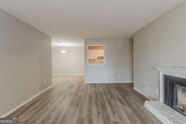 unfurnished living room with visible vents, baseboards, a fireplace with raised hearth, and wood finished floors