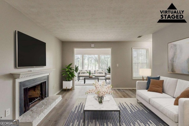 living room with a textured ceiling, wood finished floors, baseboards, and a fireplace with raised hearth