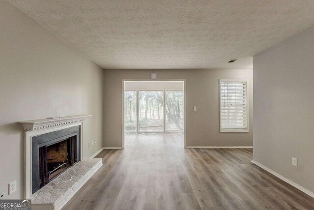 unfurnished living room with plenty of natural light, a fireplace with raised hearth, baseboards, and wood finished floors