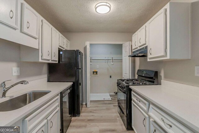 kitchen with white cabinets, a sink, under cabinet range hood, black appliances, and light wood-style flooring