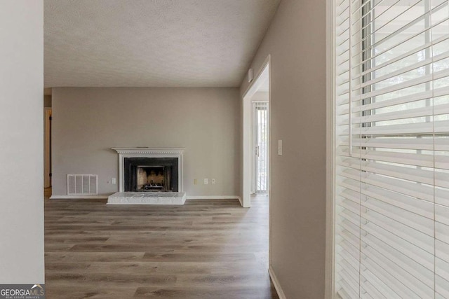 unfurnished living room with baseboards, a textured ceiling, a fireplace with raised hearth, visible vents, and wood finished floors