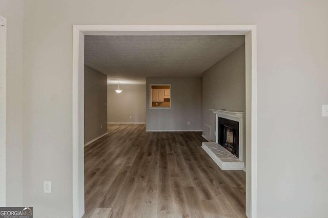 unfurnished living room featuring a textured ceiling, visible vents, a fireplace with raised hearth, wood finished floors, and baseboards